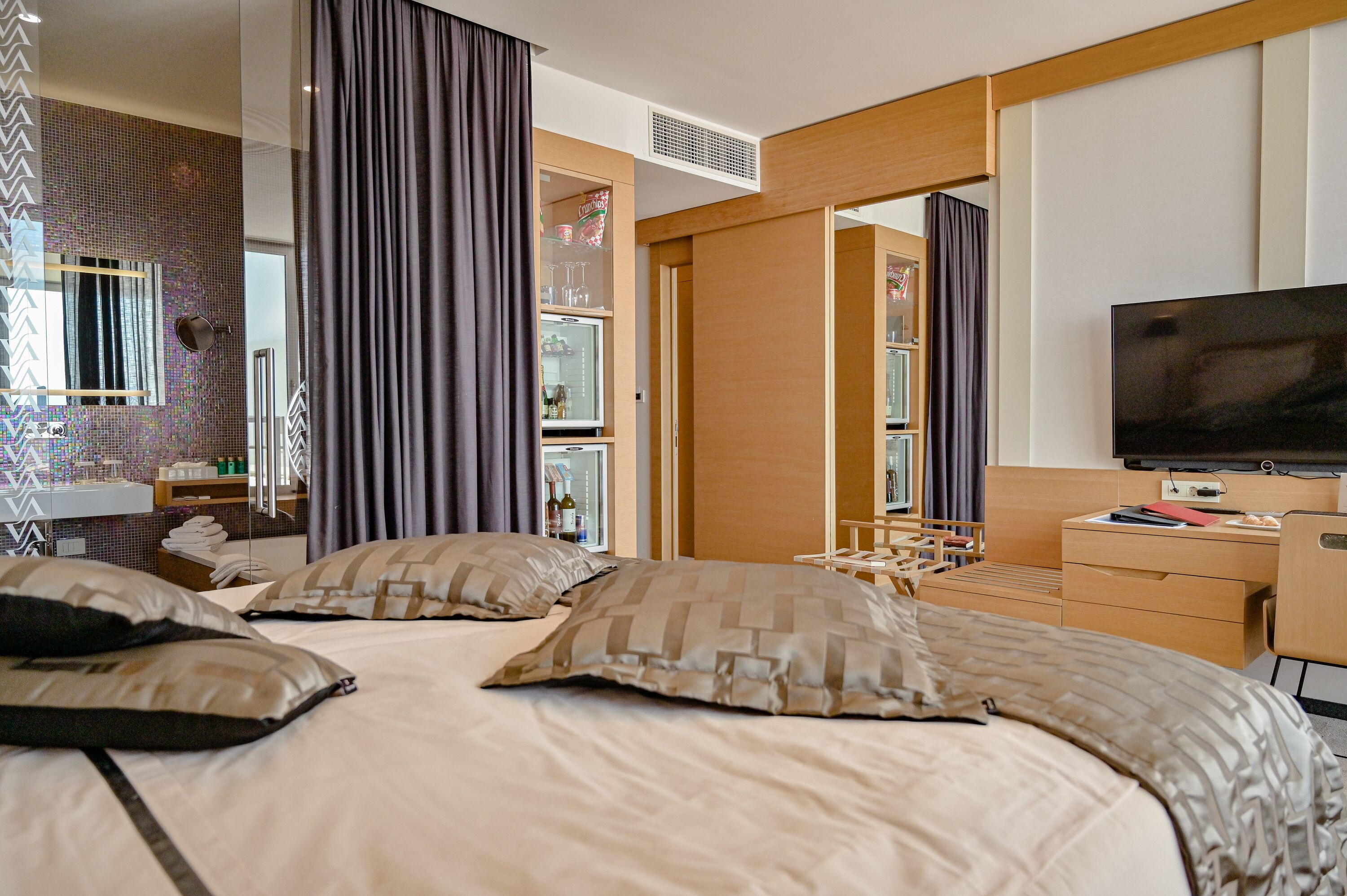 A hotel room with a bed, a TV, a desk, and a minibar.