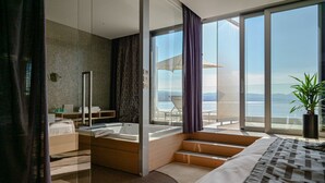 Una habitación de hotel moderna con una cama grande, un baño con bañera y un balcón con vistas al mar.