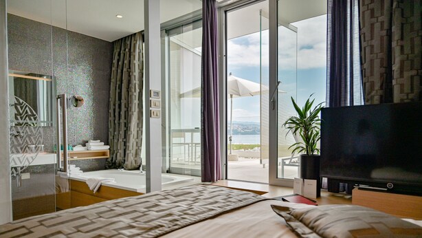 A modern hotel room with a large bed, a television, a bathroom with a glass door, and a view of the outdoors. - Bevanda Hotel & Restaurant - Unique Adriatic (Opatija)