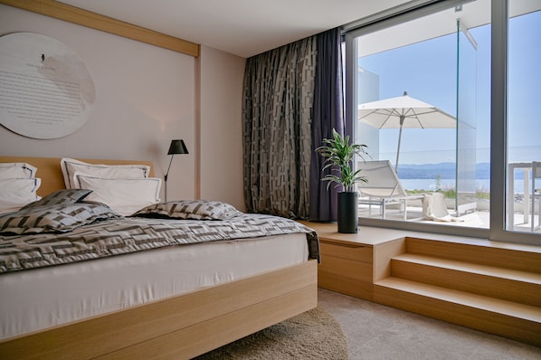 Une chambre moderne avec un grand lit, une table de chevet, une plante en pot et une vue sur l’extérieur grâce à une grande fenêtre.
