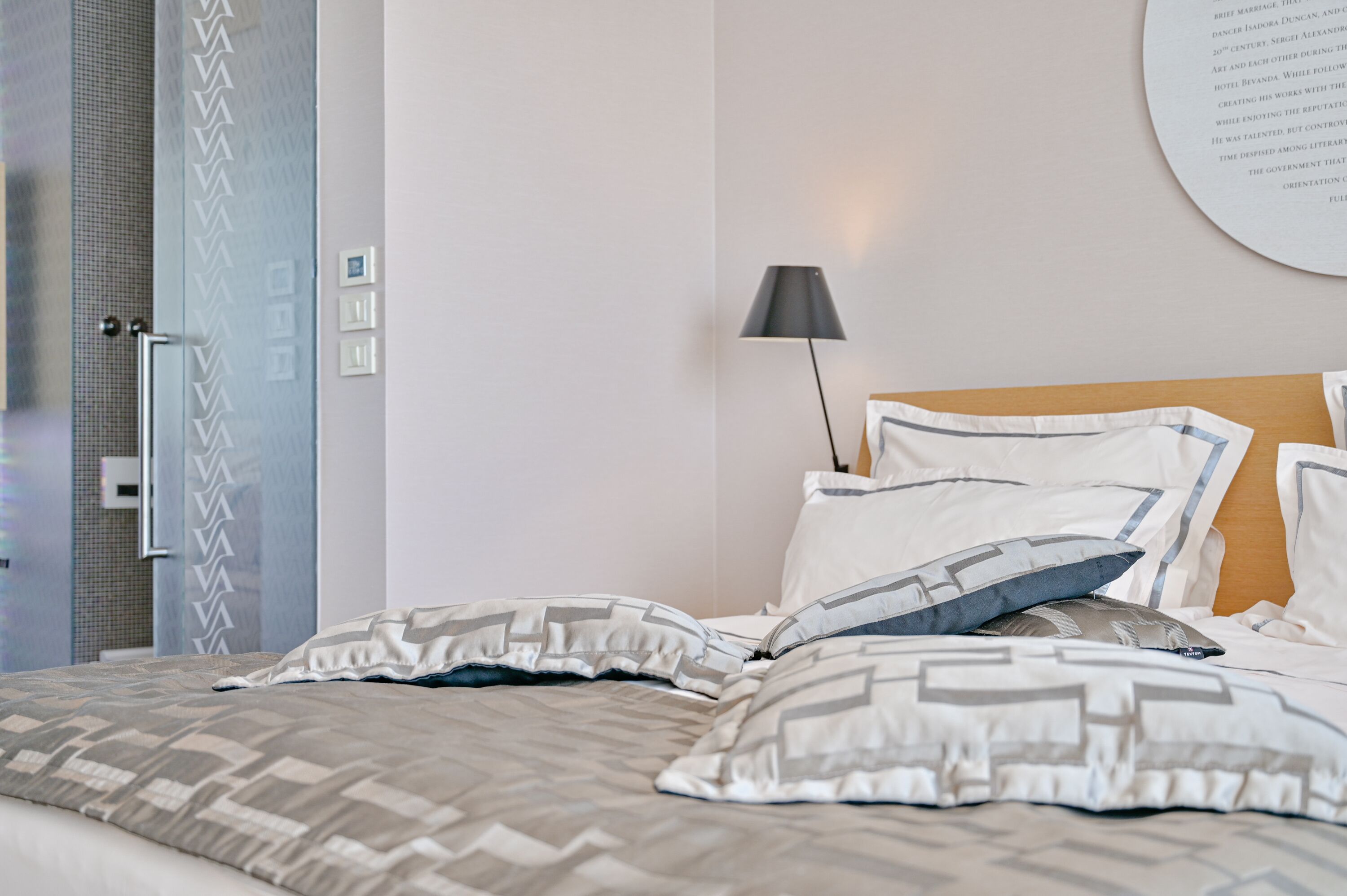 A neatly made bed with patterned pillows, a bedside lamp, and a wall with a circular informational display.