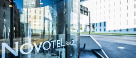 Un letrero de hotel con el nombre "NOVOTEL Basel City" y el reflejo del horizonte urbano.