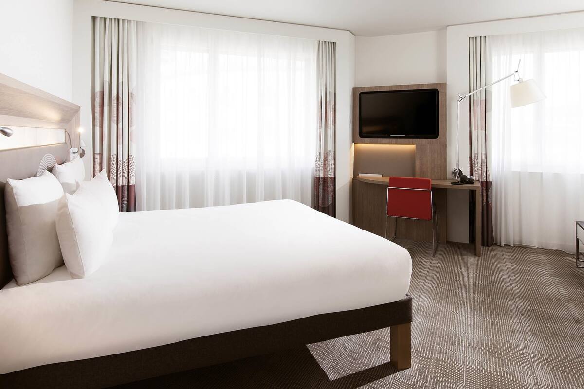 A hotel room with a large bed, a desk, a TV, and a lamp.