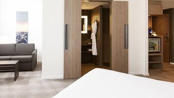 Habitación de hotel con cama, sofá gris, armario de madera y bata colgada en la puerta.