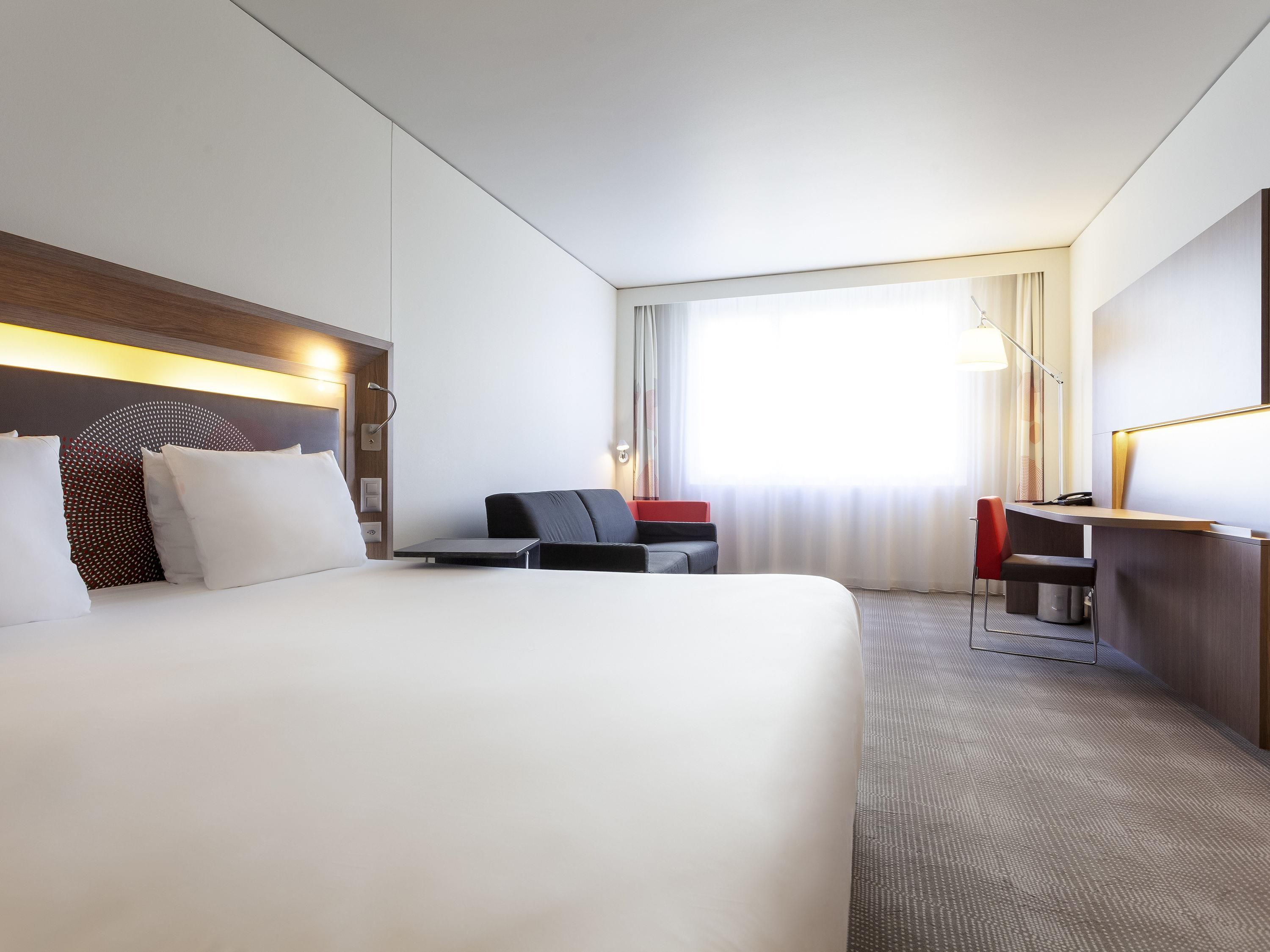 A hotel room with a large bed, a desk, a chair, and a window with curtains.