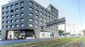 A modern hotel building with a flat facade, multiple windows, and a visible entrance. - Novotel Basel City (Basel)