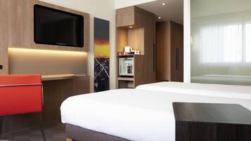 Quarto de hotel moderno com uma cama grande, televisão de tela plana na parede, uma pequena escrivaninha com cadeira e um refrigerador.