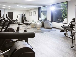 Une salle de sport équipée de tapis de course, d’appareils de musculation et de ballons d’exercice.