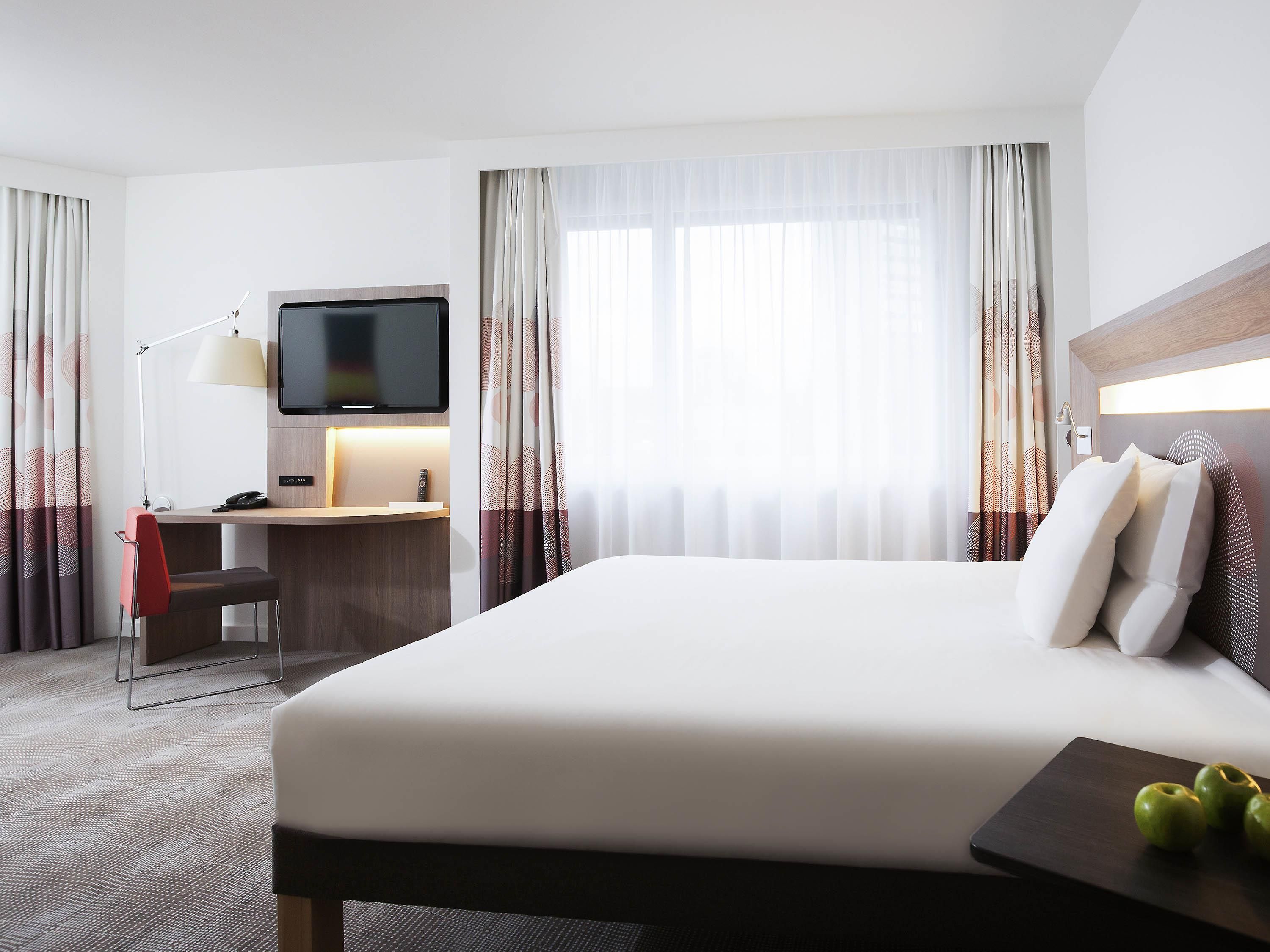 Een hotelkamer met een bed, bureau, stoel, televisie en gordijnen.