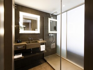 A modern bathroom with a large mirror, two sinks, a shower, and a glass-enclosed shower area. - Novotel Basel City (Basel)
