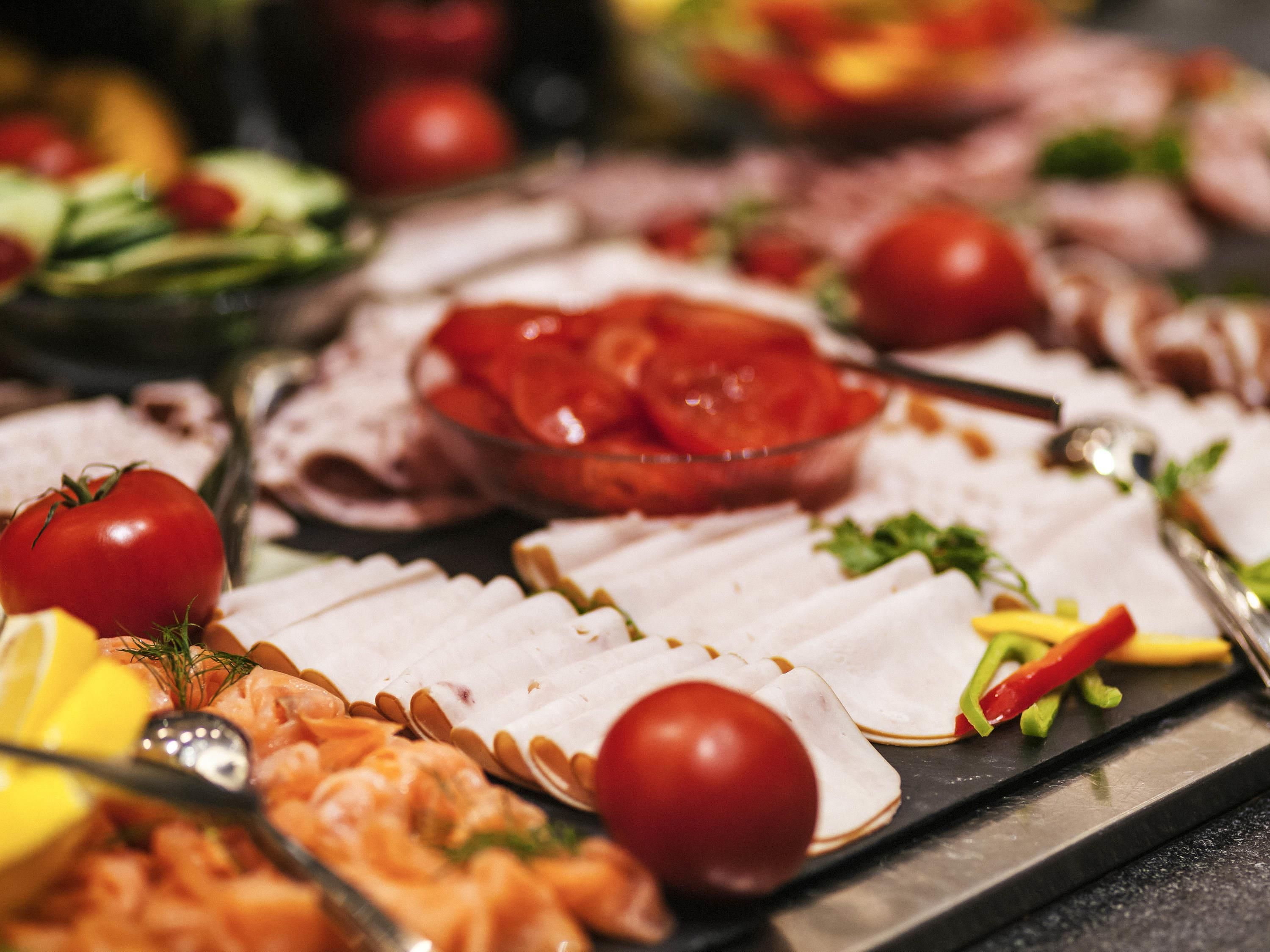 A buffet with various food items including sliced meats, vegetables, and a bowl of tomatoes.