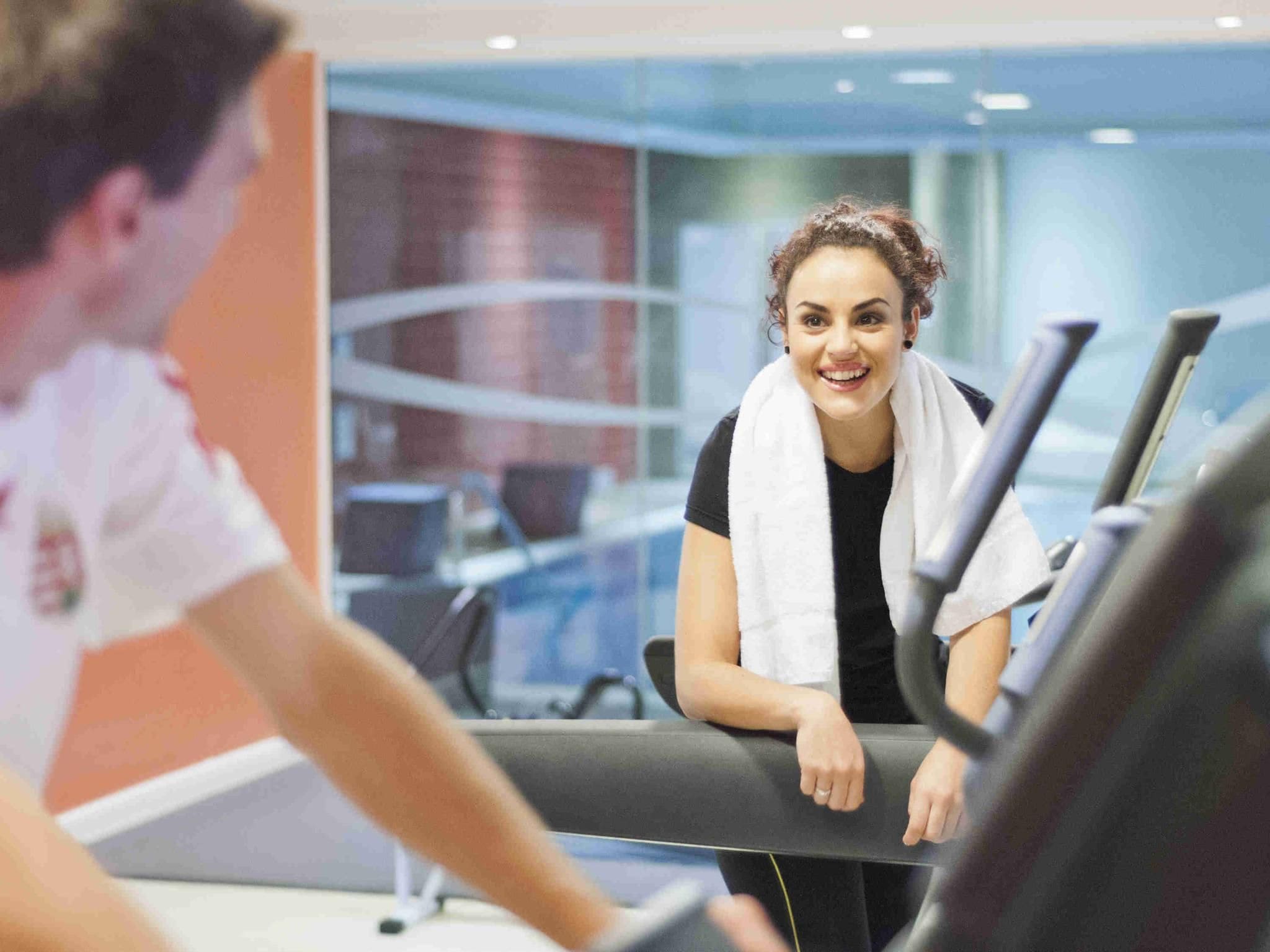 Una persona usando una cinta de correr en un gimnasio con un muro de cristal y una ventana al fondo.