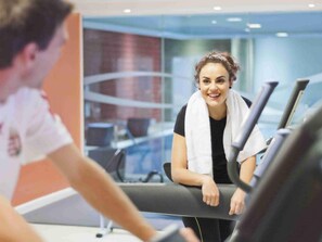 A person using a treadmill in a gym with a glass wall and a window in the background.