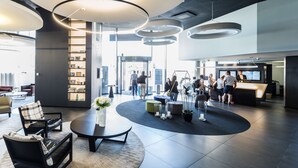 A modern lobby with a reception desk, seating area, and a large circular rug. - Novotel Basel City (Basel)