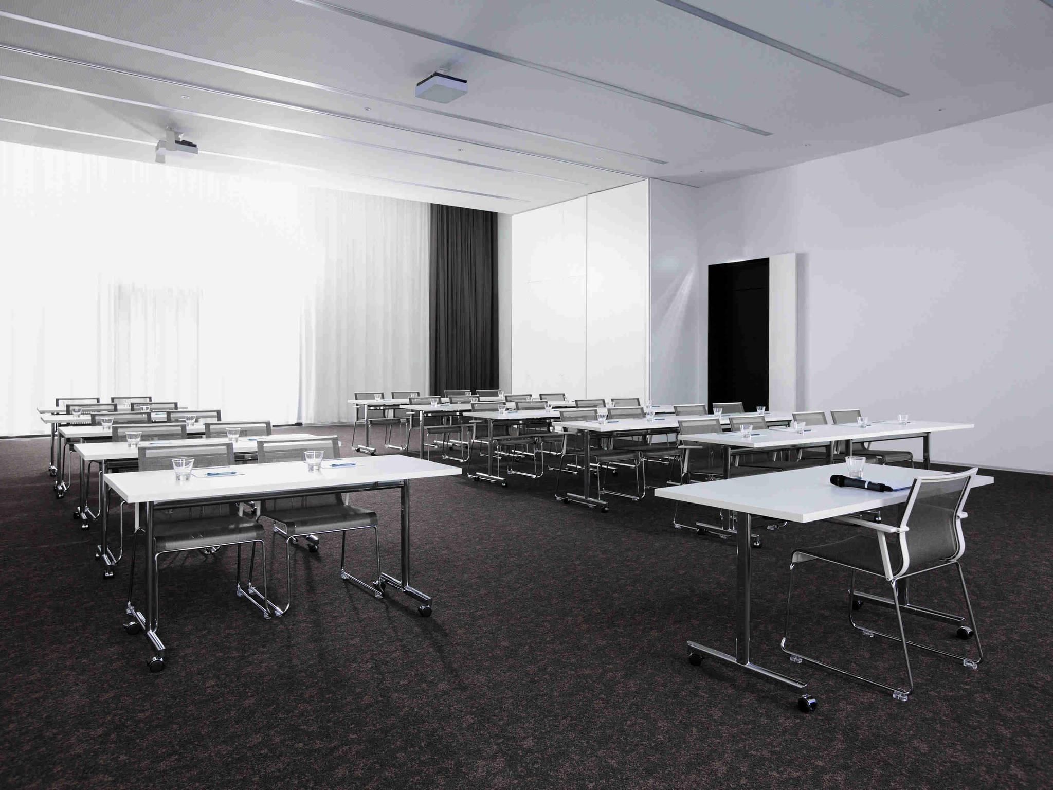 A conference room with multiple tables, chairs, and a projector screen.
