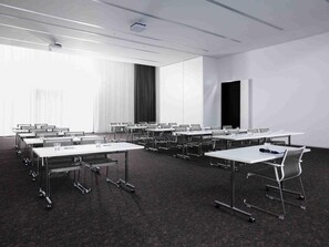Un salón de conferencias con varias mesas, sillas y una pantalla para proyector.