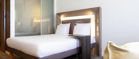 Una habitación de hotel moderna con una cama grande, una mesita de noche y un separador de vidrio.