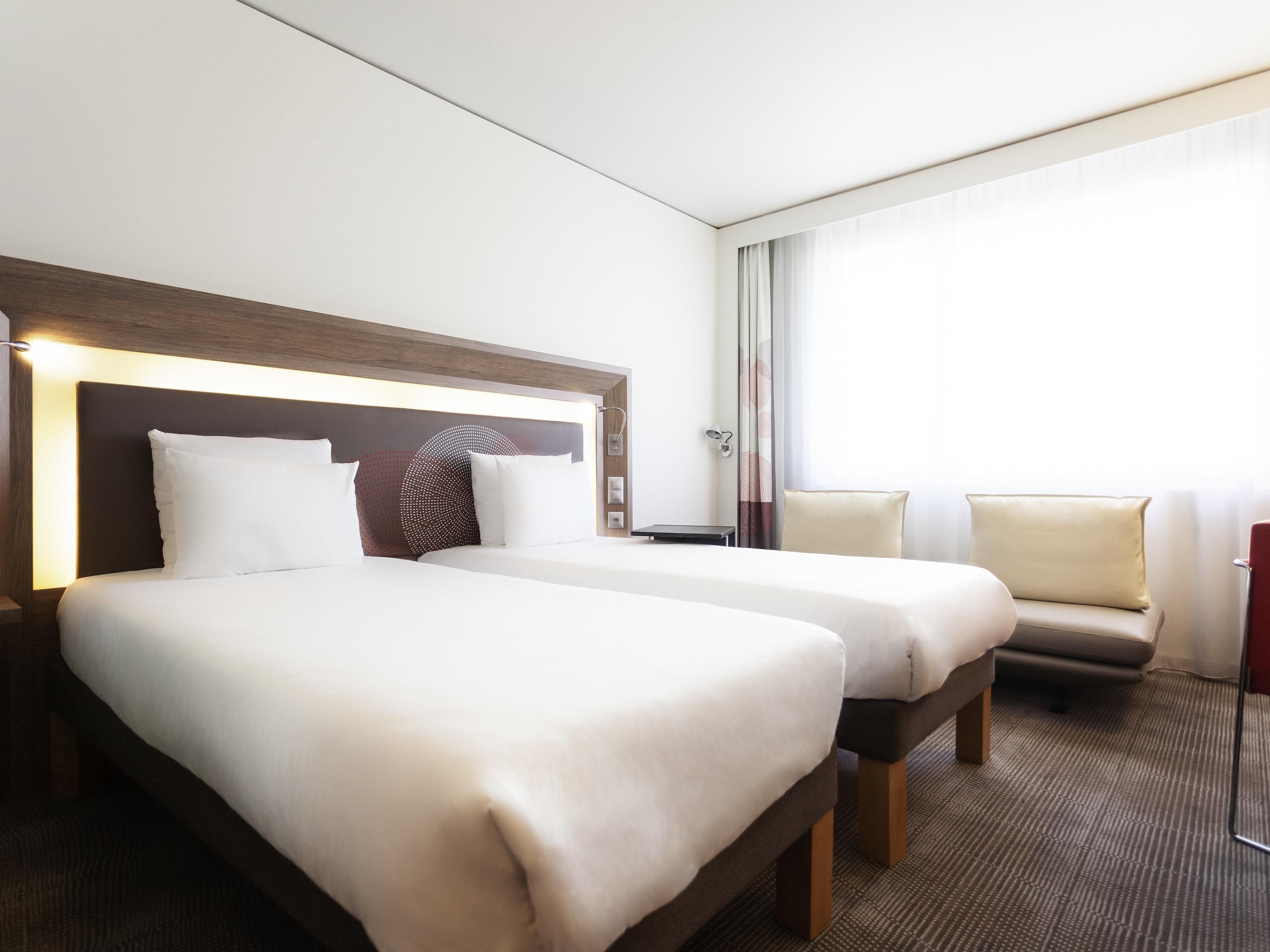 A hotel room with two beds, a sofa, a desk, and a large window.