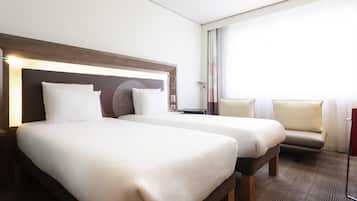A hotel room with two beds, a sofa, a desk, and a large window.