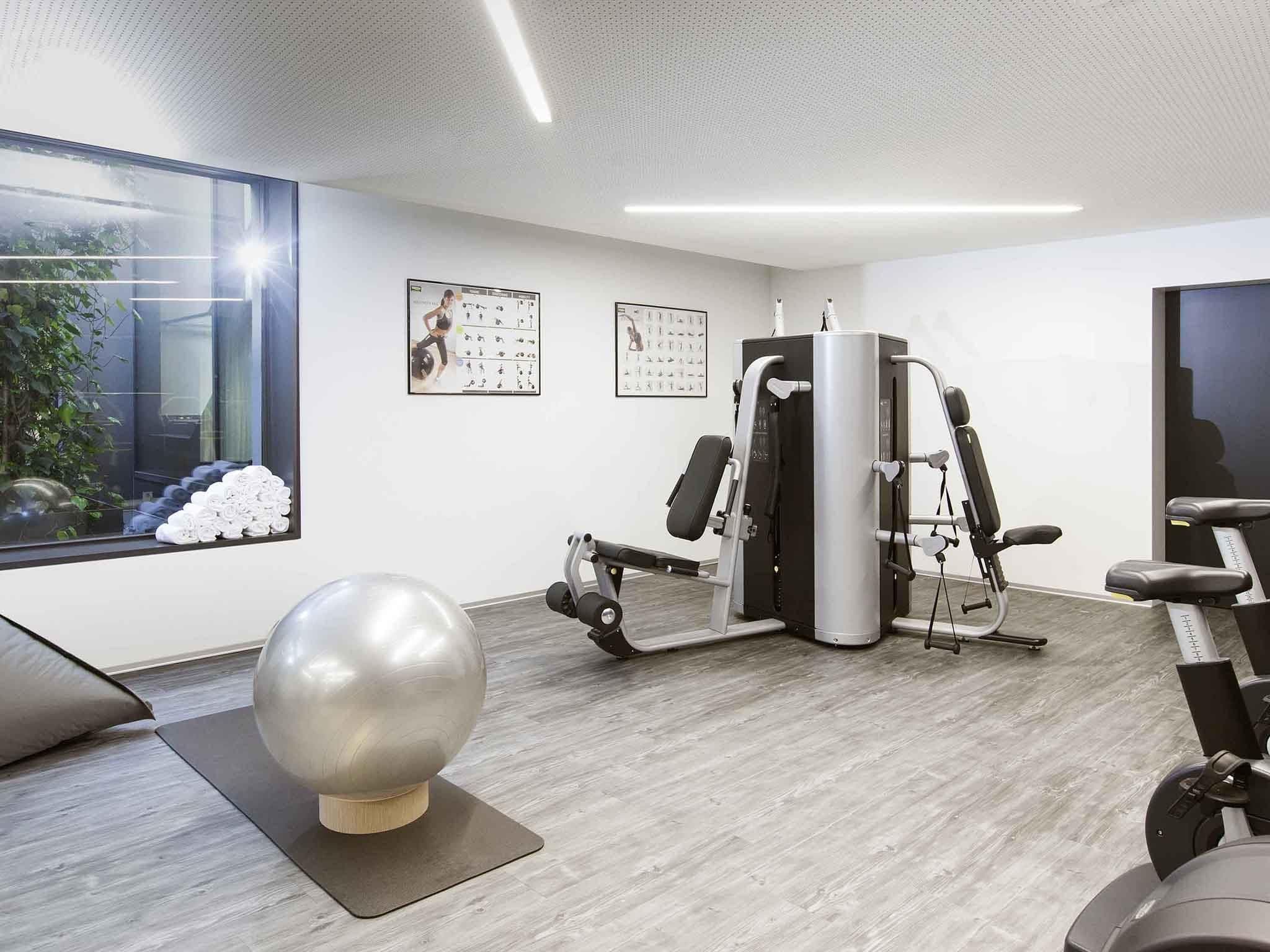 Un gimnasio moderno con equipo de ejercicio, una pelota de ejercicio grande y un ventanal con vistas a la vegetación.