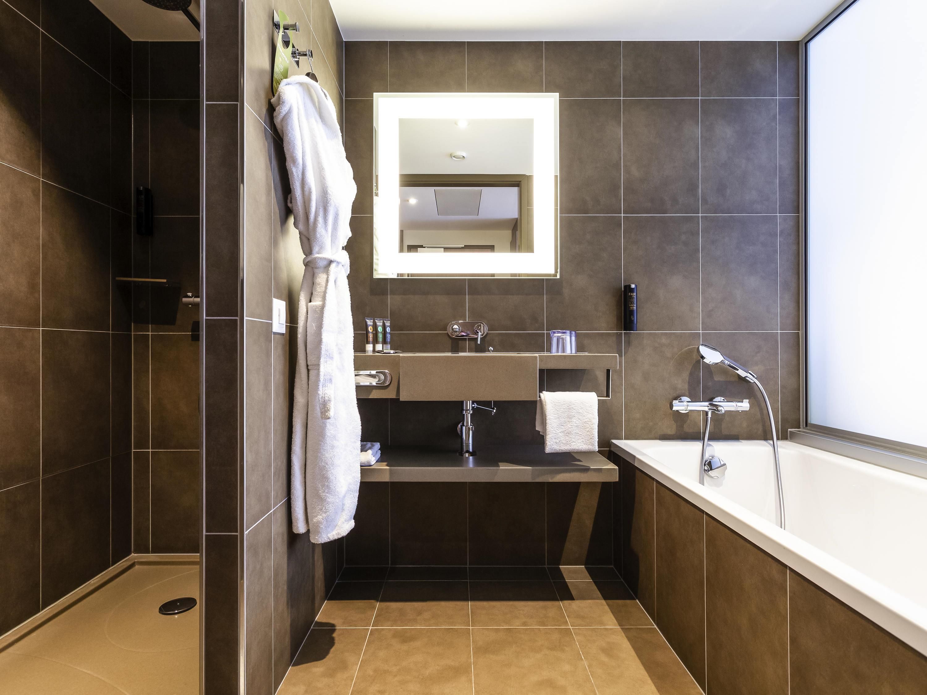 Un baño moderno con ducha a ras de suelo, bañera y un espejo grande sobre el lavabo.