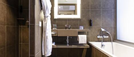 Un baño moderno con ducha a ras de suelo, bañera y un espejo grande sobre el lavabo.
