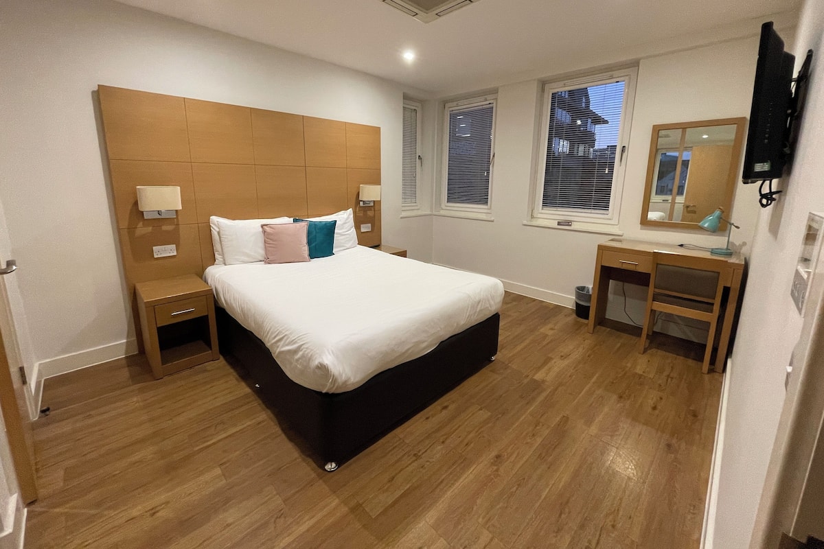 Une chambre à coucher avec un grand lit, une tête de lit en bois, des tables de chevet, un bureau et un miroir.