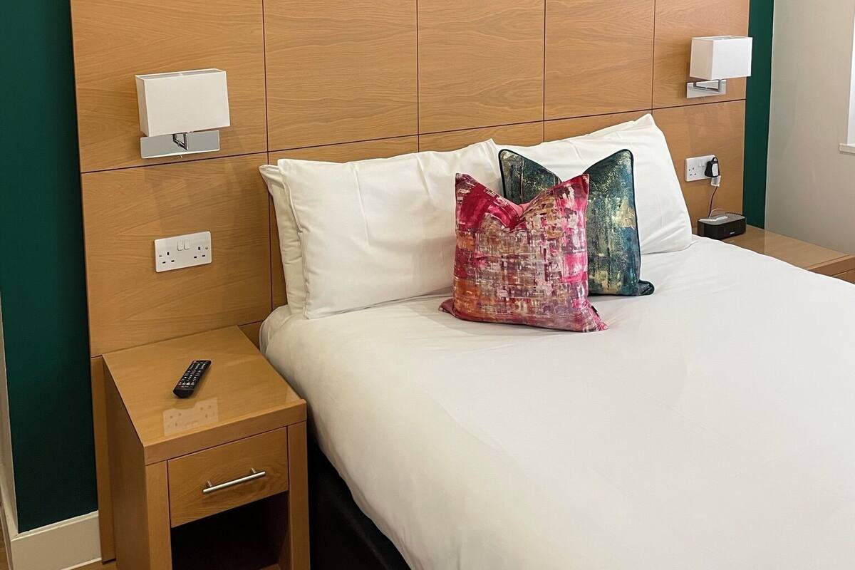 Une chambre d’hôtel avec un grand lit, deux tables de chevet, une tête de lit en bois et deux lampes fixées au mur.