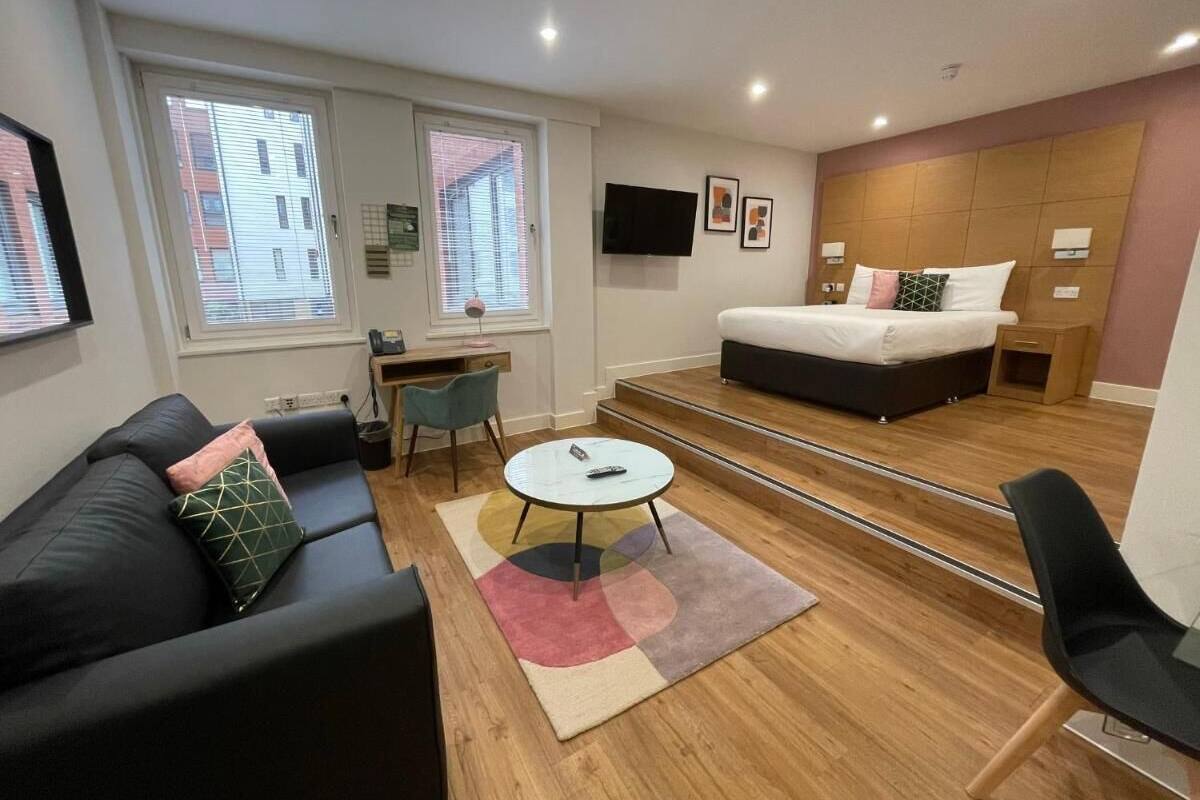 Une chambre d’hôtel moderne, équipée d’un canapé, d’une table basse ronde, d’un lit et d’un téléviseur fixé au mur.