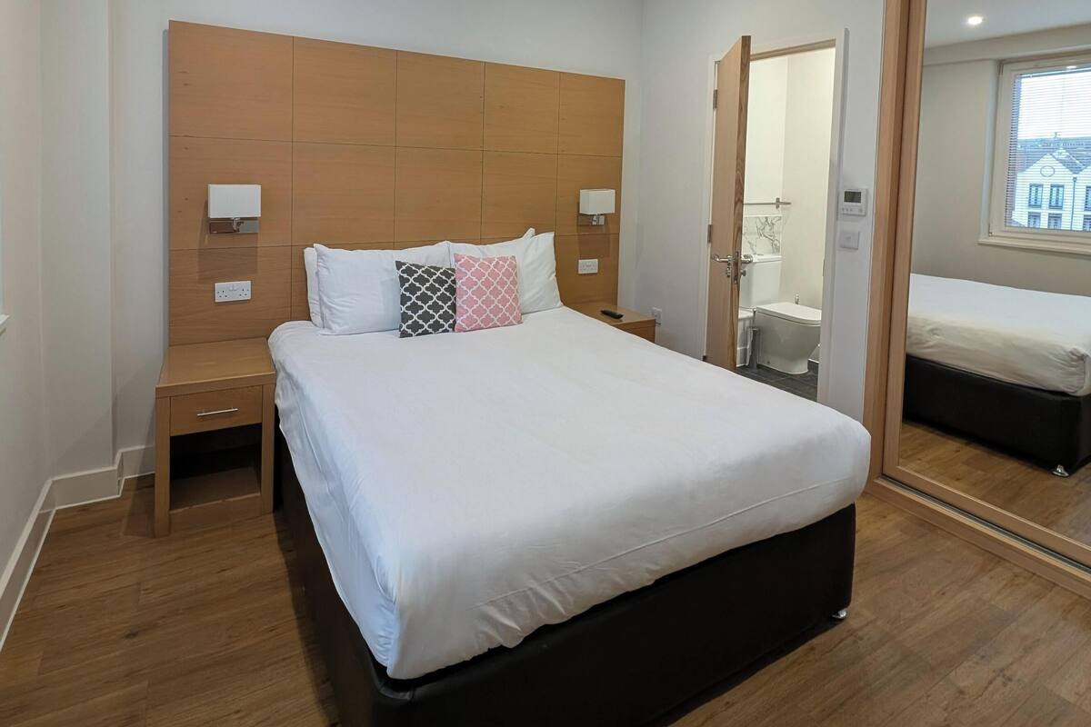 Une chambre moderne avec un grand lit, une tête de lit en bois, des tables de chevet et un miroir.