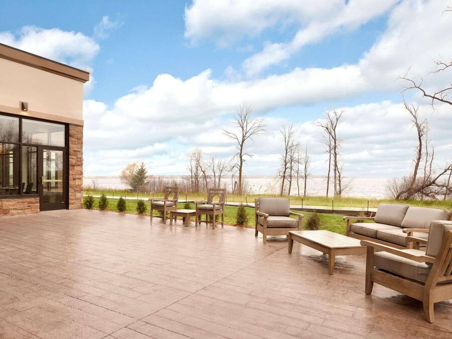 An outdoor patio with wooden furniture, a stone floor, and a view of a lake and trees.
