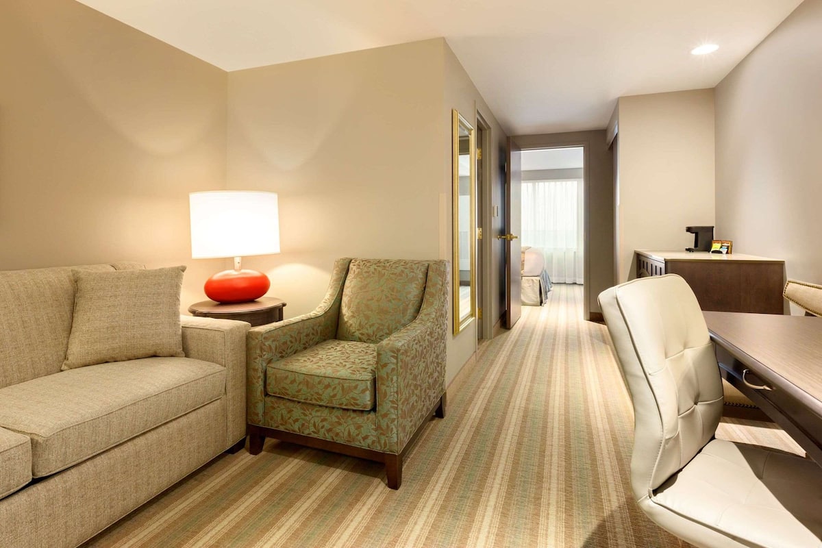 A hotel room with a sofa, armchair, and a dining table with chairs.