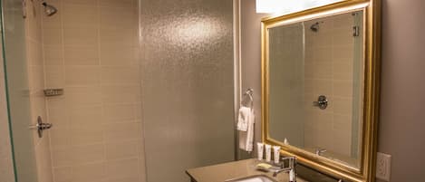 A bathroom with a shower, sink, and large mirror.