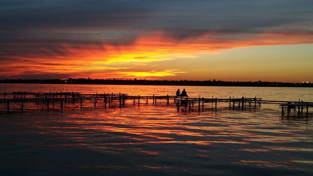 A sunset over a calm body of water with a pier extending into the water. - Country Inn & Suites by Radisson, Bemidji, MN (Bemidji)