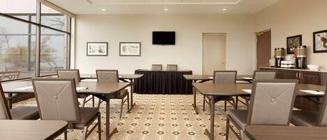 Un salón de conferencias con una gran mesa, varias sillas, un televisor de pantalla plana y un espacio para café.