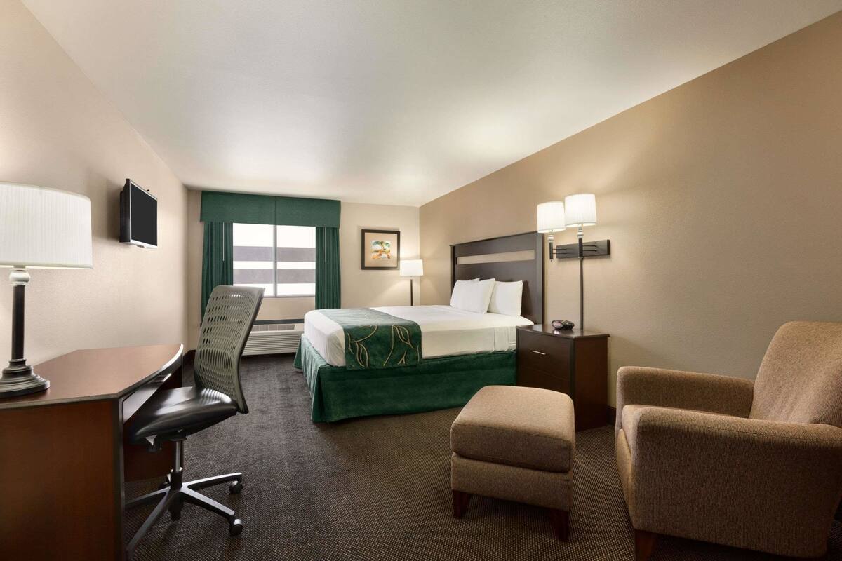 Ein Hotelzimmer mit Bett, Schreibtisch, Bürostuhl, Sessel und Nachttischlampen.