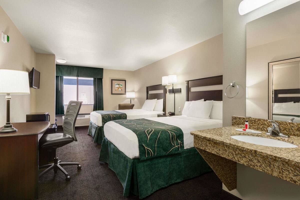 Ein Hotelzimmer mit zwei Betten, einem Schreibtisch, einem Stuhl, einem großen Spiegel und einem Badezimmer mit Waschbecken und Toilette.