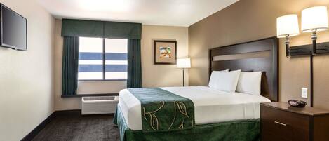 A hotel room with a bed, a desk, a lamp, a picture on the wall, and a window with curtains.