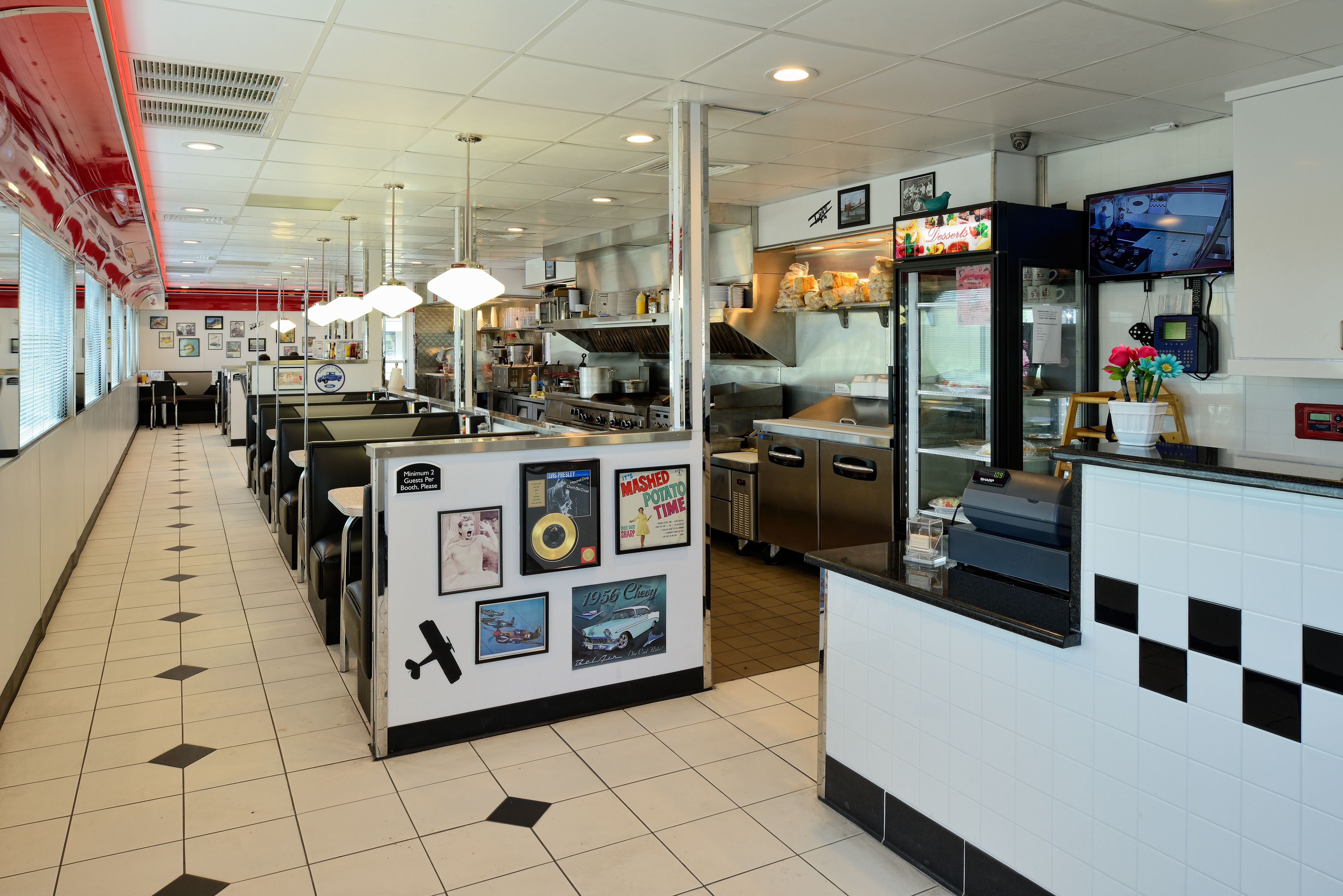 A restaurant with a long counter, multiple tables, and a kitchen area with stainless steel appliances.
