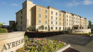 A multi-story hotel with a beige facade, a landscaped entrance, and a clear sky. - Ayres Hotel Orange (Orange)