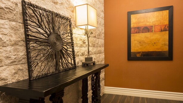 A stone wall with a decorative metal piece and a framed painting. - Ayres Hotel Orange (Orange)