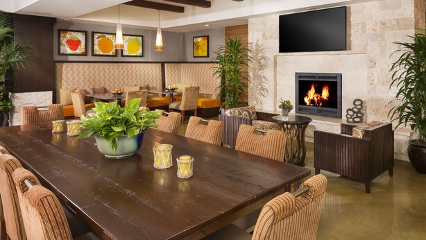 A spacious living area with a large wooden table, comfortable seating, a fireplace, and decorative plants. - Ayres Hotel Orange (Orange)