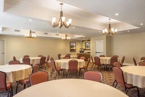 A conference room with multiple tables and chairs, chandeliers, and a kitchenette. - Ayres Hotel Orange (Orange)