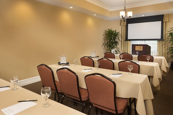 Un salón de conferencias con varias mesas, sillas y una pantalla para proyector.