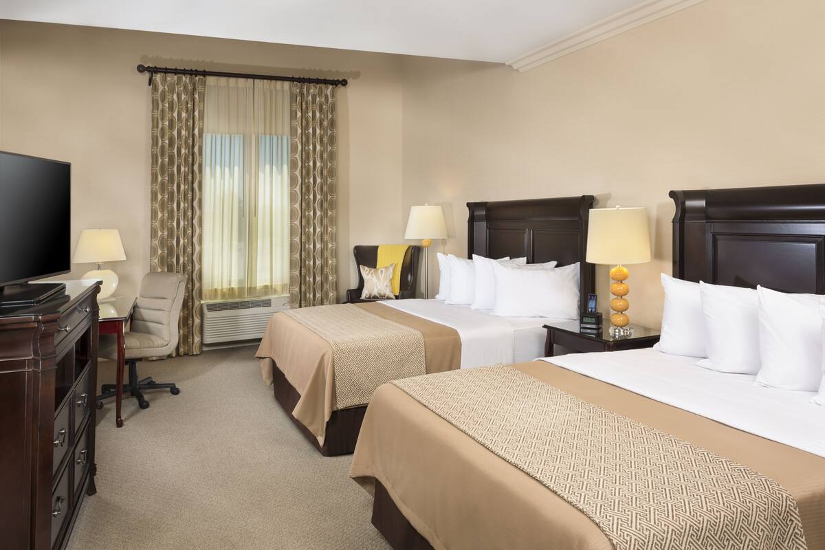A hotel room with two beds, a desk, a TV, and a window with curtains.