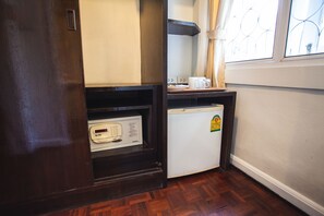 A compact kitchen with a microwave, a small refrigerator, and a window with curtains. - The Sunrise Residence (Bangkok)