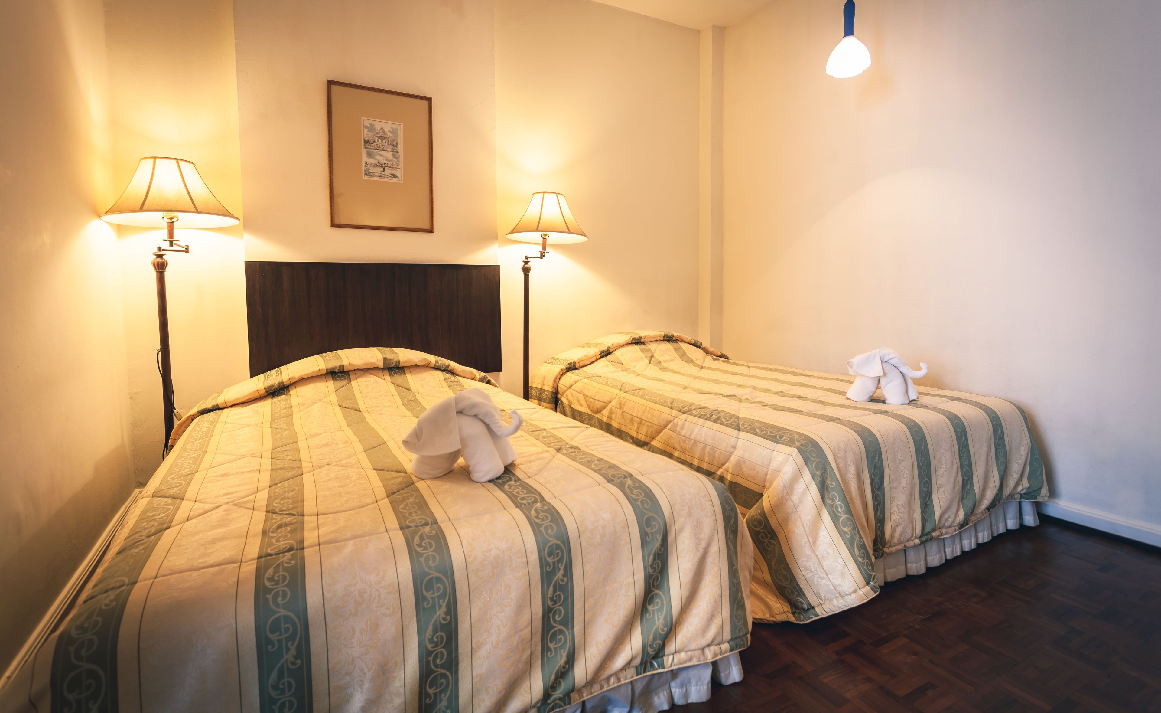 Deux lits simples avec du linge de lit à rayures, un tableau encadré au mur et deux lampadaires.