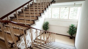 Una escalera con barandales de metal ornamentados y pasamanos de madera, que conduce a una plataforma con dos plantas en macetas.