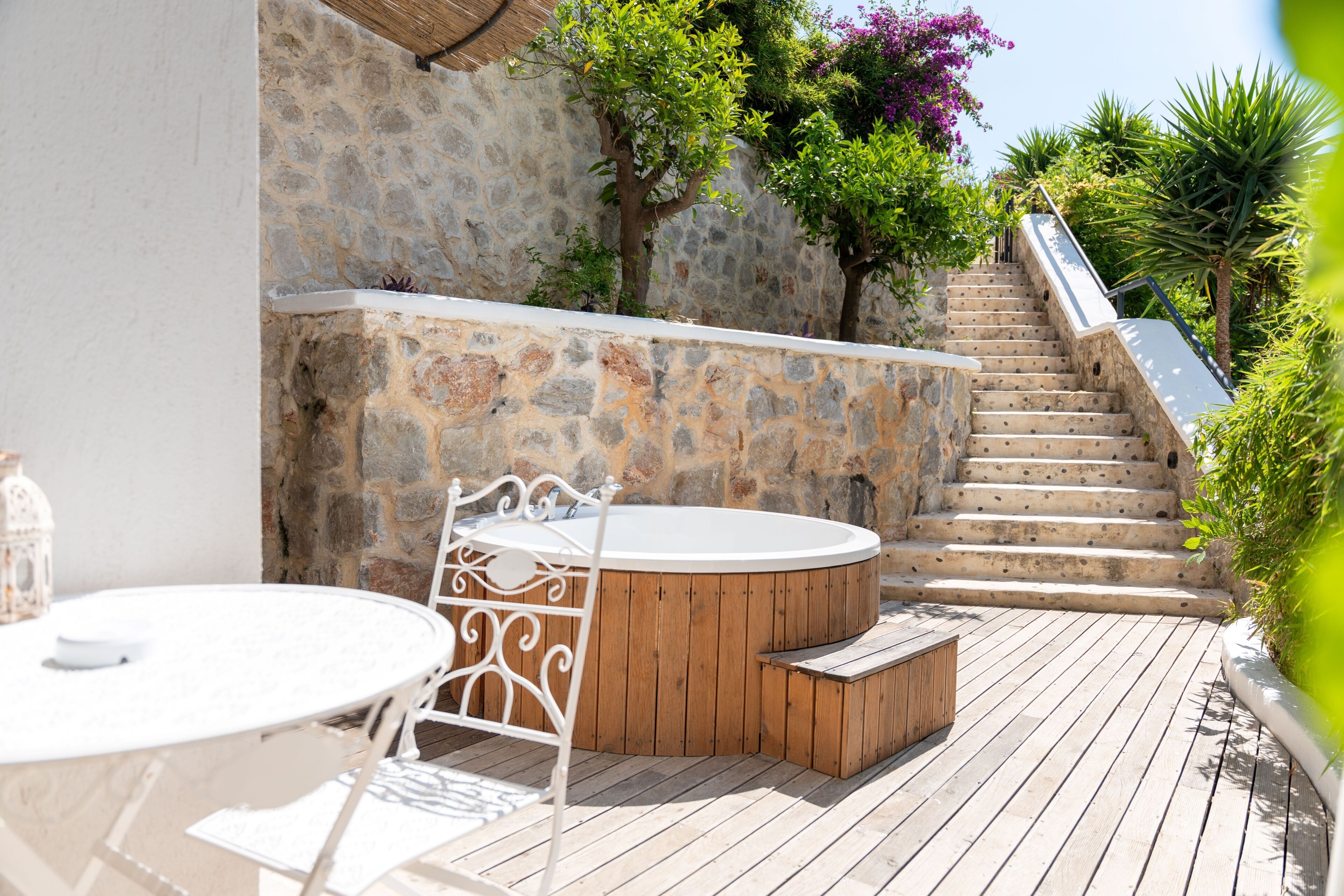 A stone wall, a wooden staircase, and a round wooden hot tub with a bench.