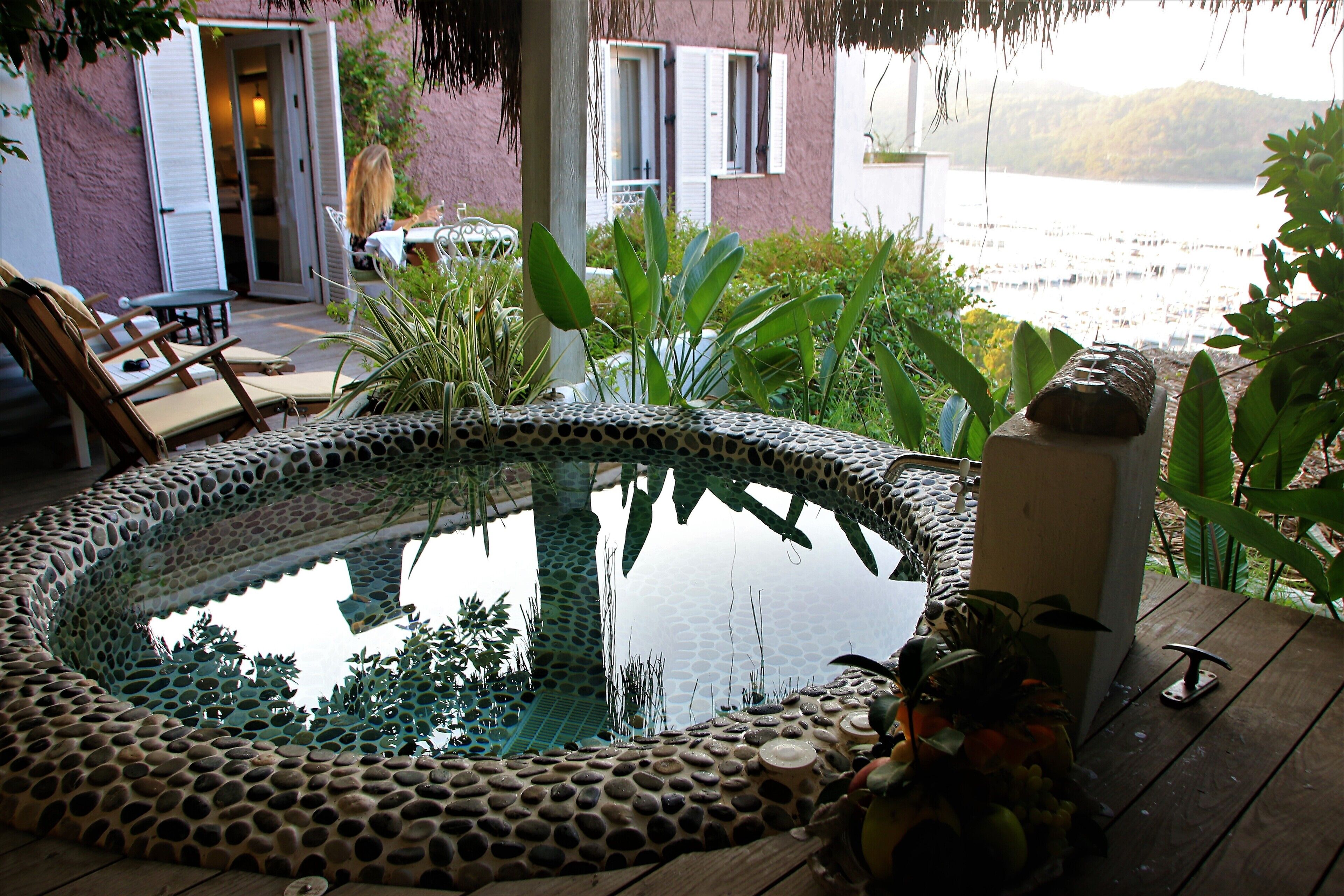 Een hottub omringd door planten, een houten terras en uitzicht op een waterpartij.